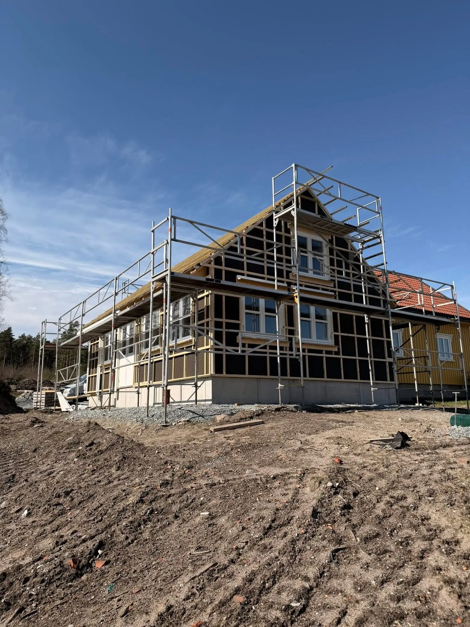Det nye bygget med vindsperre, lekter og stillas ved siden av den gule kårboligen
